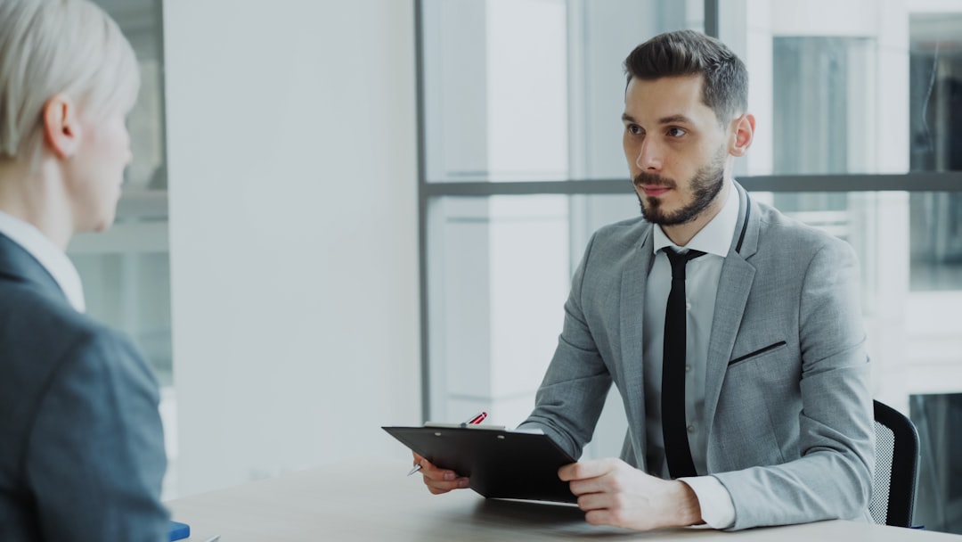 HR male manager having job interview with young woman in suit and watching her resume application in modern office indoors